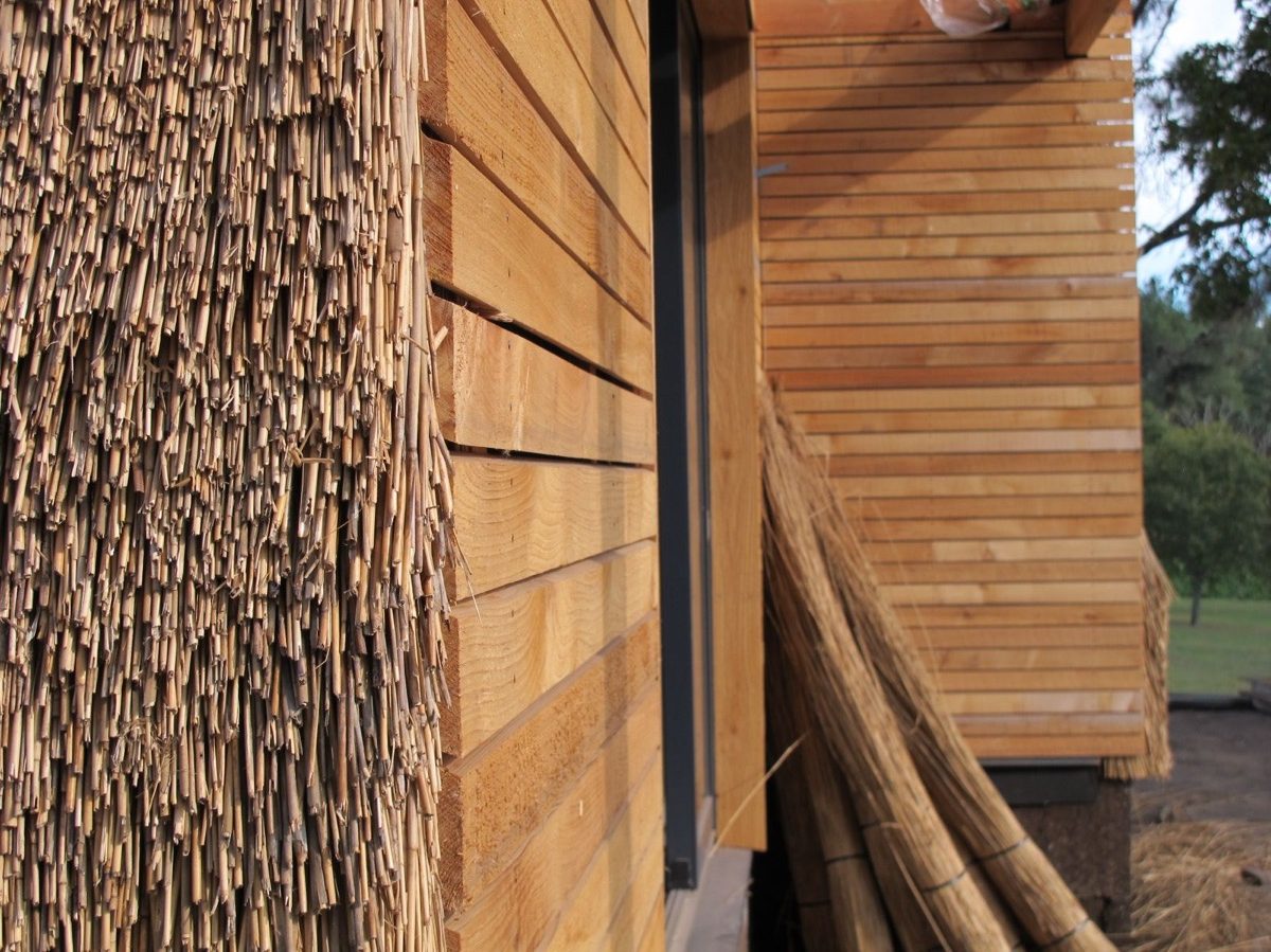 Finition extérieure de la maison entre bardage bois et roseaux en façade
